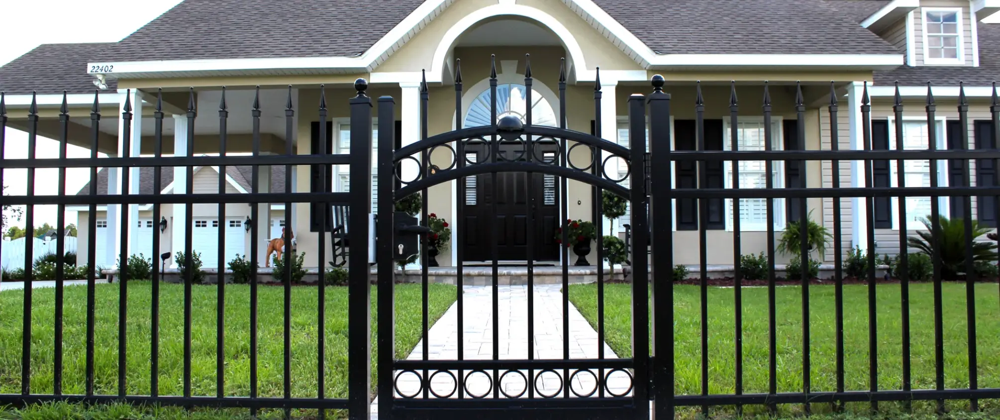 Decorative black aluminum driveway gate in front of suburban home entrance