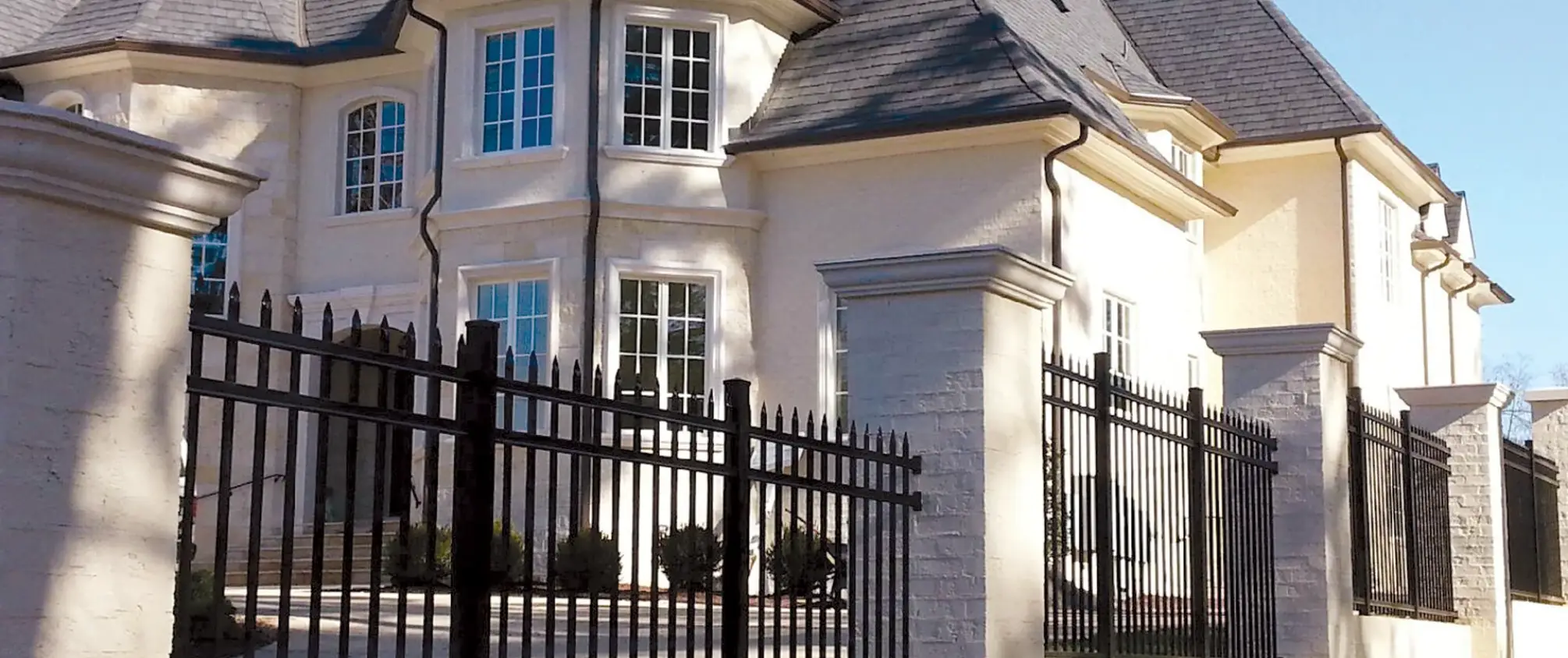 Luxury home with black aluminum fence and stone pillars along front yard