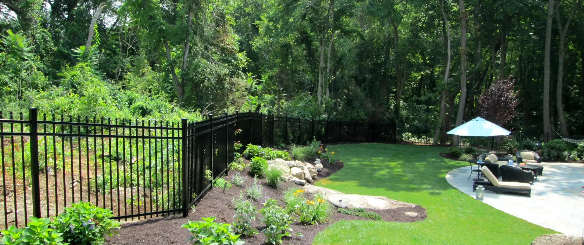 Black aluminum fence bordering landscaped backyard with patio seating area